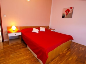 A neatly made bed with a red bedspread and two pillows, a bedside table with a lamp, and a small nightstand. - Apartments Milano 994 (Fazana)