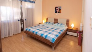 Un dormitorio con una cama de madera, dos mesitas de noche con lámparas, un ventanal con cortinas y una pared decorada con un cuadro.