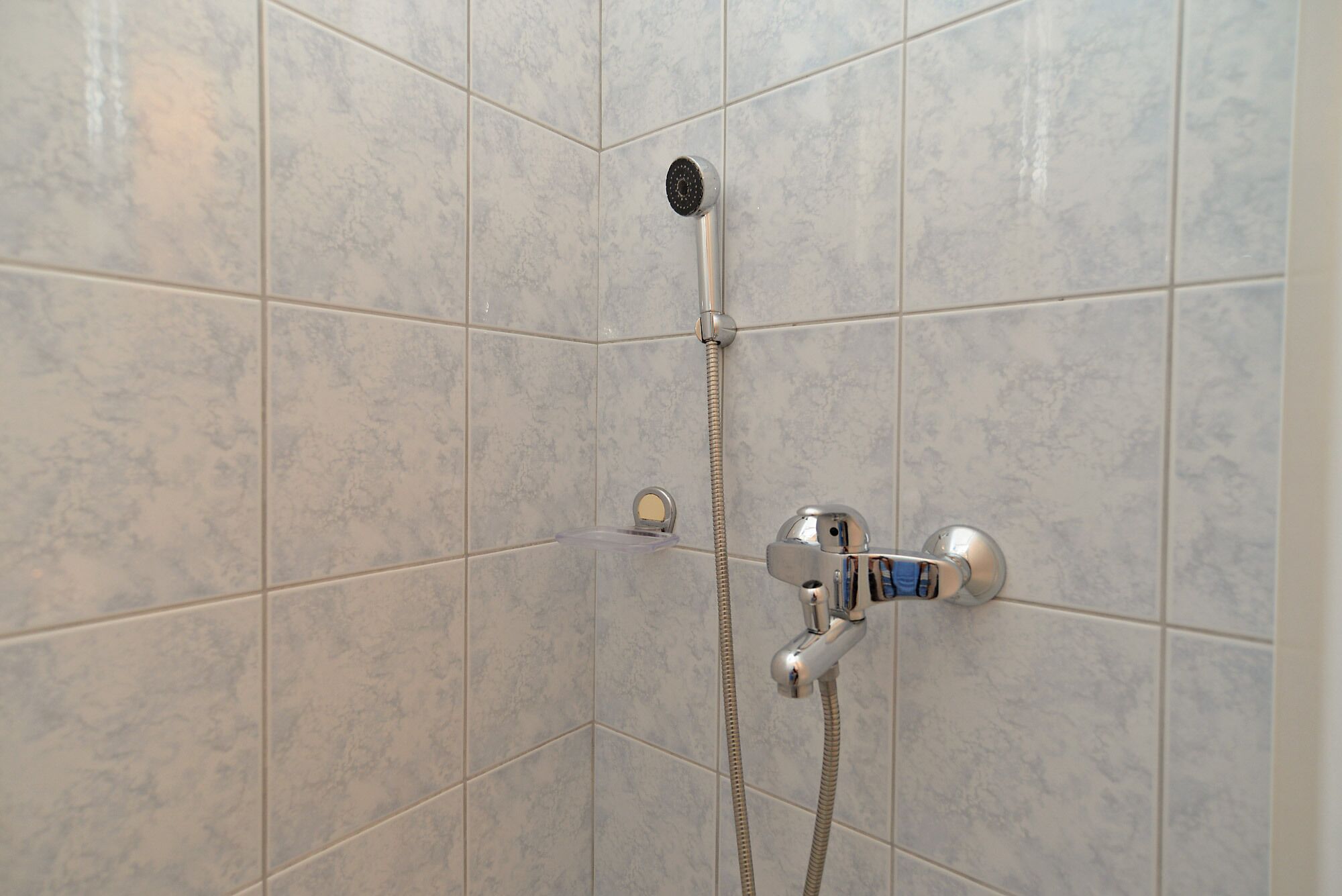 Eine Dusche mit Duschkopf zum Händelhalten und einem wandmontierten Wasserhahn.