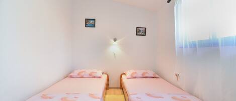A small, clean room with two wooden beds, a wall-mounted light, and two small pictures.