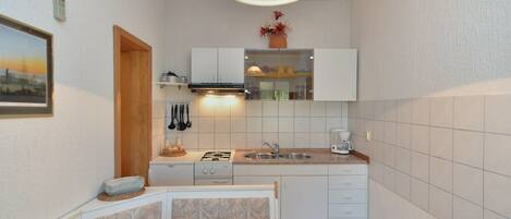 Cocina compacta con armarios blancos, un lavamanos, una estufa y una zona de comedor con una mesa y sillas.