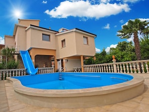 Um edifício de dois andares com piscina, um escorrega azul e uma varanda com guarda-corpo.