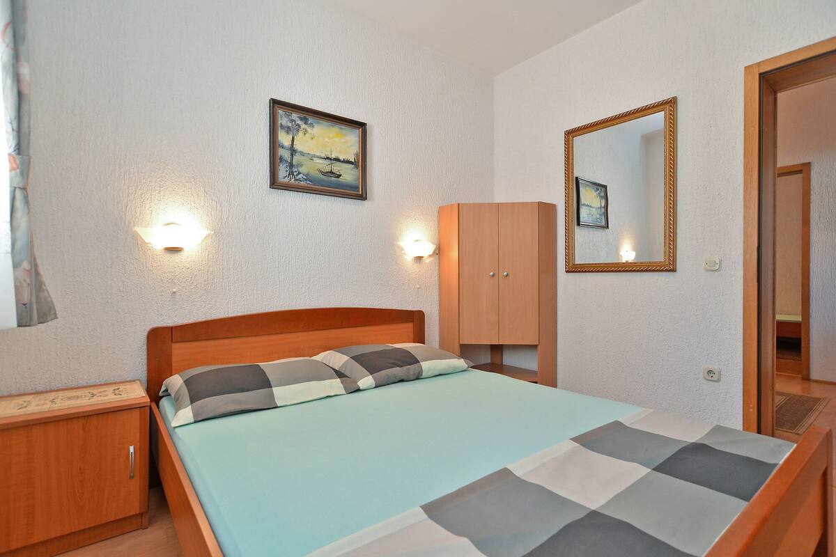 A bedroom with a bed, wooden wardrobe, and a painting on the wall.