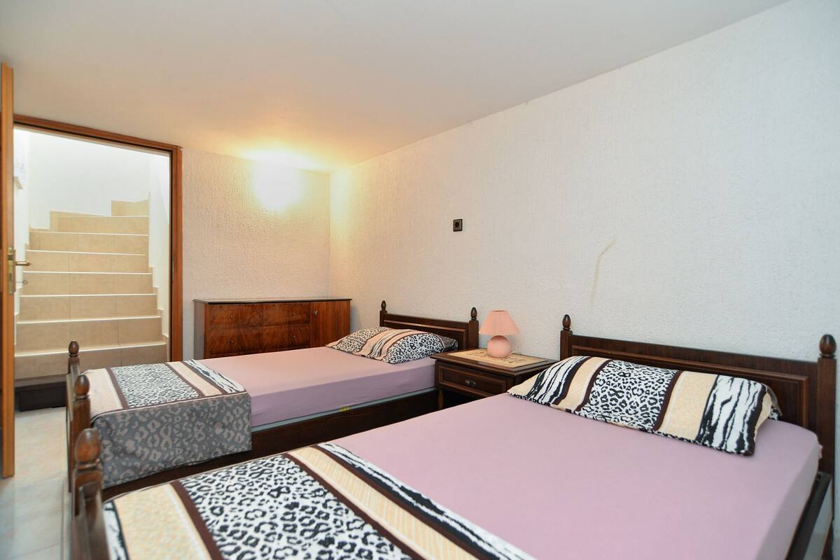 A hotel room with two beds, a wooden headboard, a nightstand, a lamp, and a staircase leading to an upper floor.