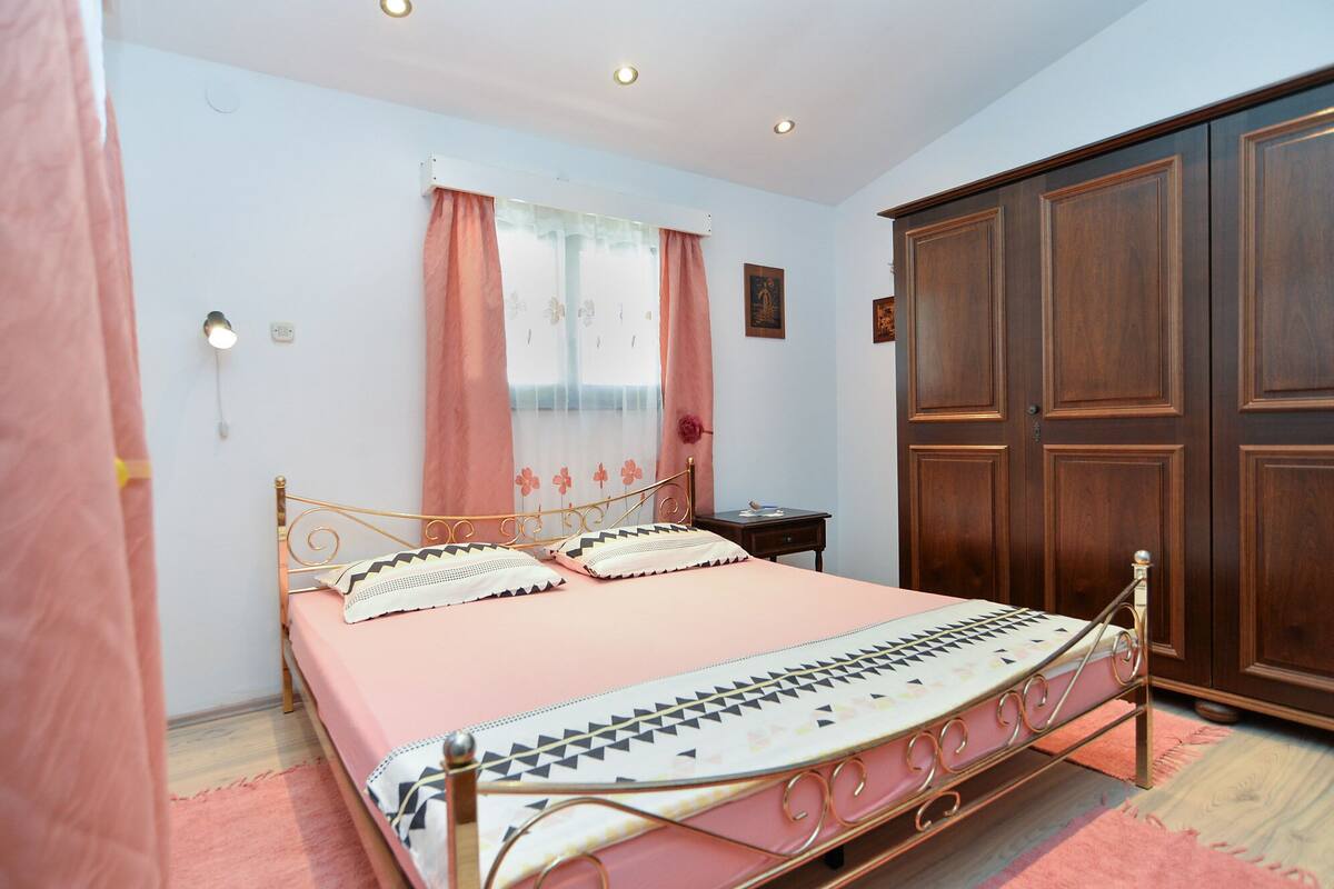 A bedroom with a bed, a wardrobe, a nightstand, and a window with curtains.