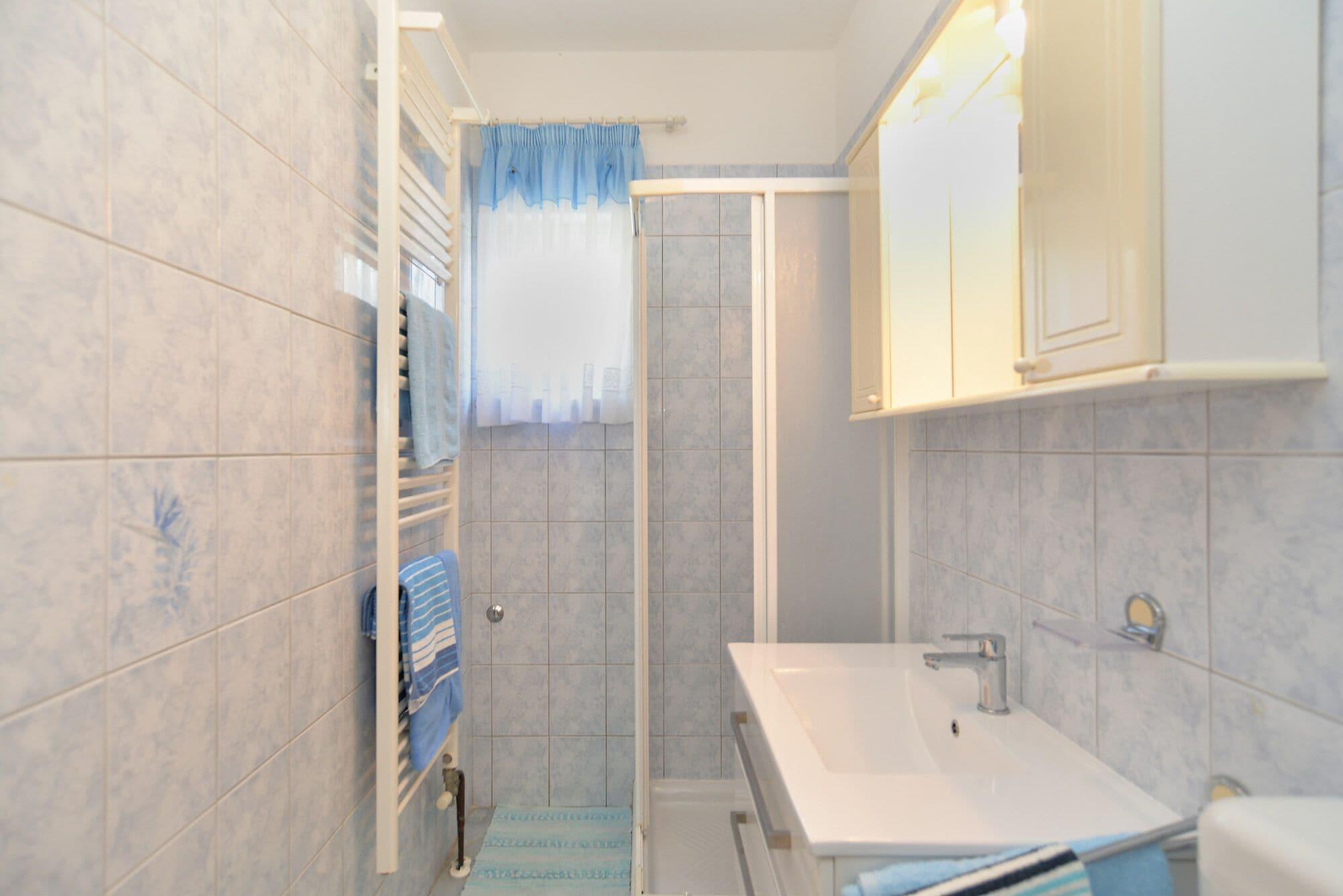 A bathroom with a shower, a sink, and a towel rack.