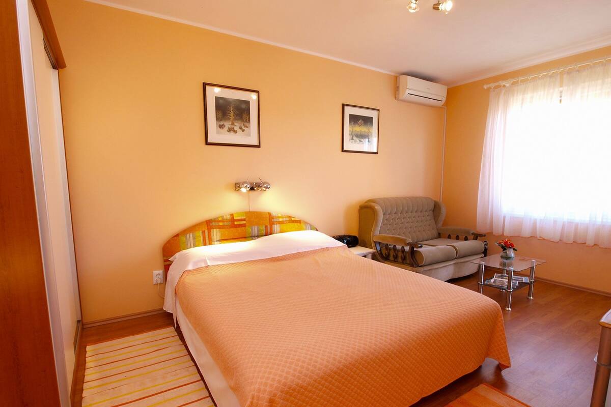 Habitación de hotel con una cama grande, una silla, una mesita y dos cuadros en la pared.