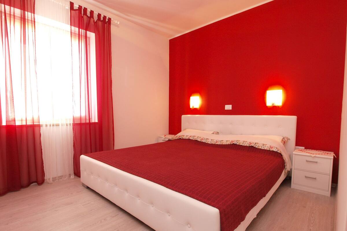 Un dormitorio con cama blanca, cortinas rojas y dos lámparas de noche.