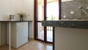 Une cuisine compacte équipée d’un réfrigérateur, d’un évier et d’une fenêtre donnant sur un balcon.