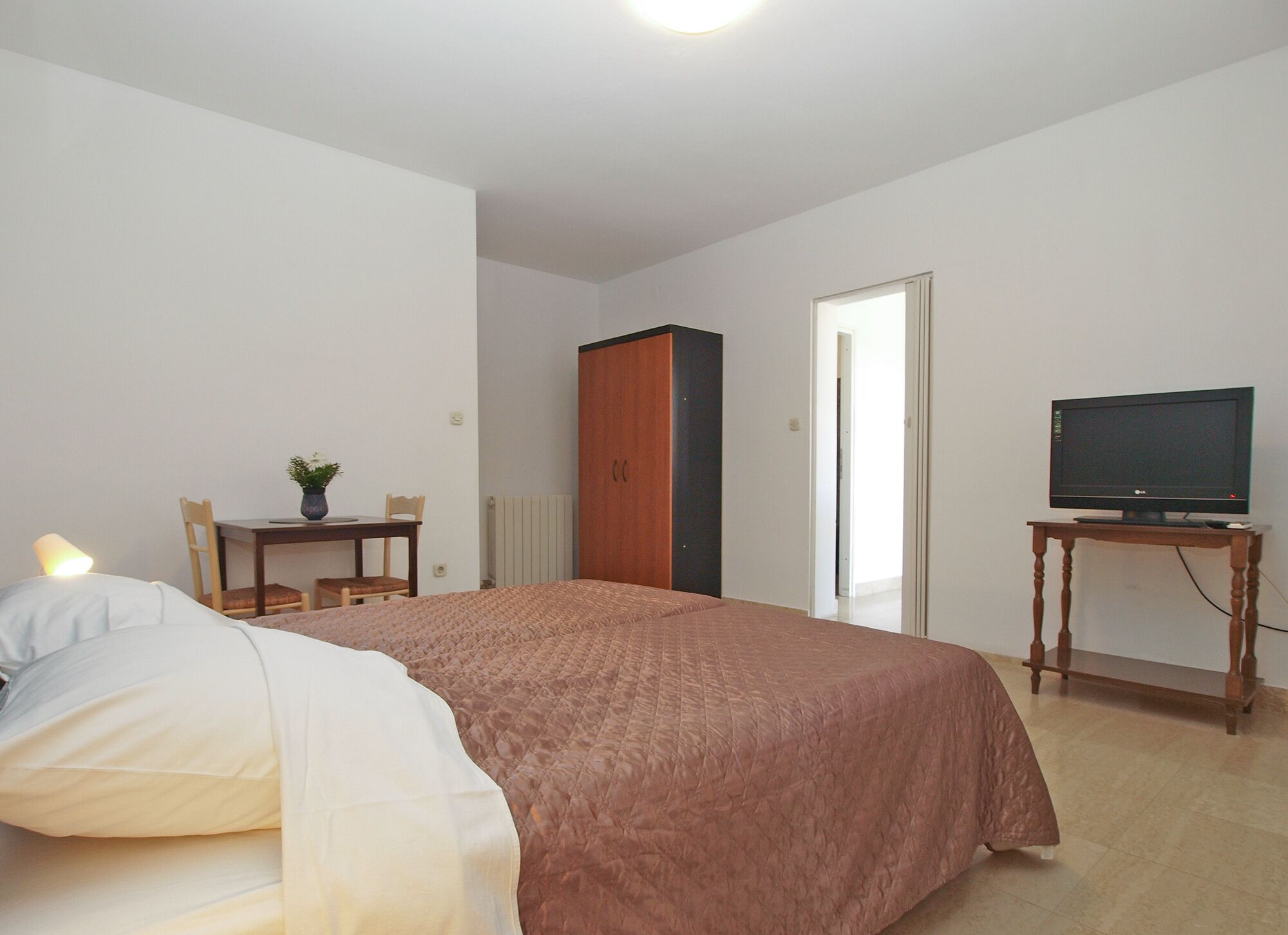 A bedroom with a bed, a desk with a chair, a television on a stand, and a wardrobe.