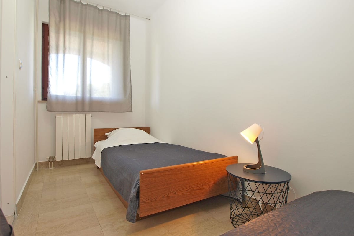 A small, neatly arranged bedroom with a single bed, a bedside lamp, and a radiator.