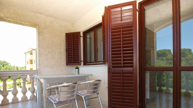 Un balcon avec une table et des chaises, des volets en bois et une vue sur la verdure.