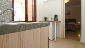 Une cuisine compacte avec une fenêtre, une machine à café et une petite plante posée sur le plan de travail.