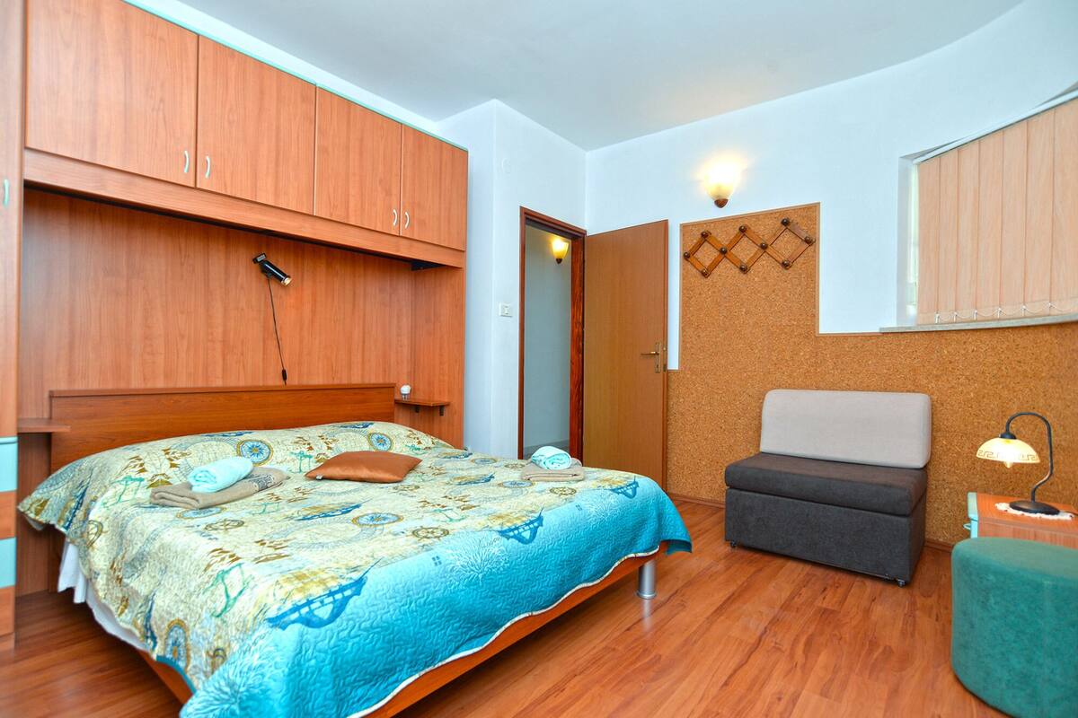 A bedroom with a bed, a chair, a desk, and a corkboard on the wall.