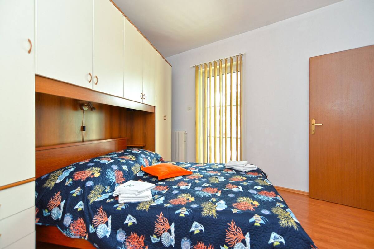 A bedroom with a bed, a wardrobe, and a window with vertical blinds.