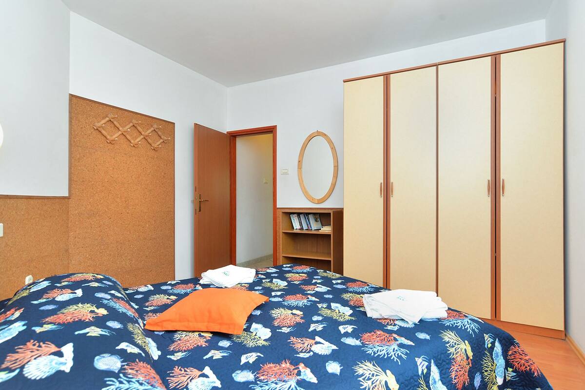 A bedroom with a bed, a wardrobe, a shelf with books, and a corkboard on the wall.