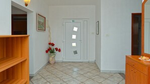 A hallway with a wooden bench, a vase with red flowers, a white door with a window, and a wooden cabinet with a mirror. - Apartments Nelli 624 (Pula)