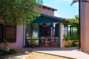A cozy outdoor dining area with a table and chairs, surrounded by plants and a building with a tiled roof. - Apartments Graziella 992 (Pula)