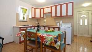 A compact kitchen with wooden cabinets, a dining table with chairs, a refrigerator, and a window with curtains. - Apartments Jacqueline 1227 (Medulin)