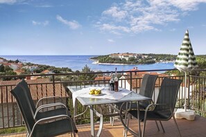 Ein Balkon mit Tisch für zwei Personen, mit Blick auf die Küste, ein Gebäude und Boote.