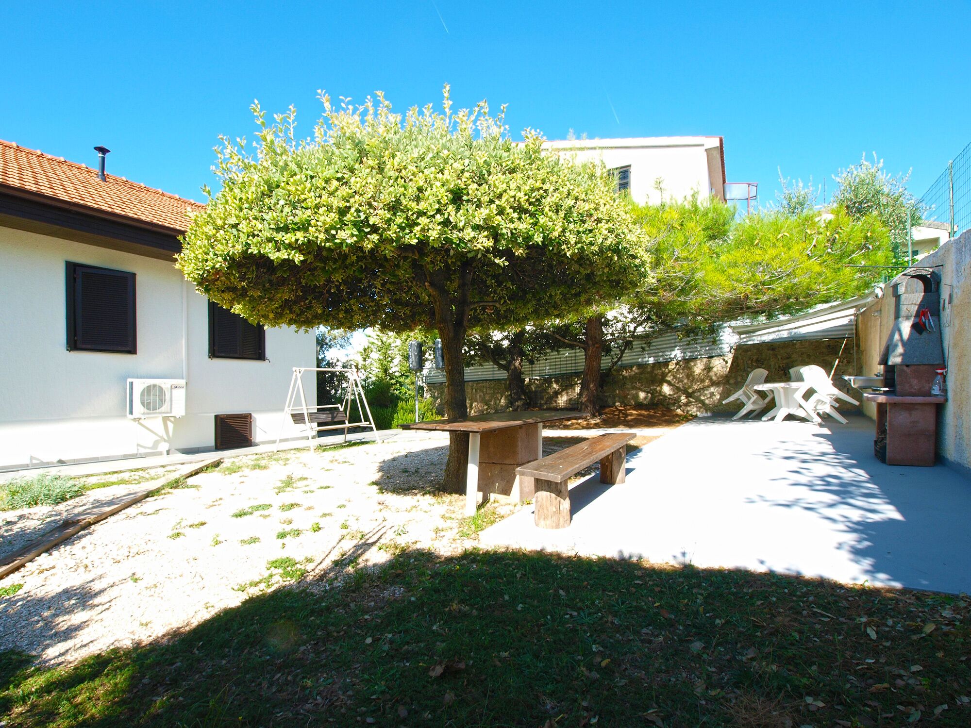 A patio area with a wooden bench, a swing set, and a barbecue grill.