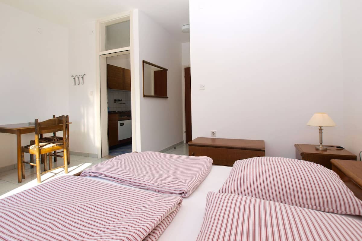 A bedroom with two beds, a desk, a chair, a nightstand, and a lamp.