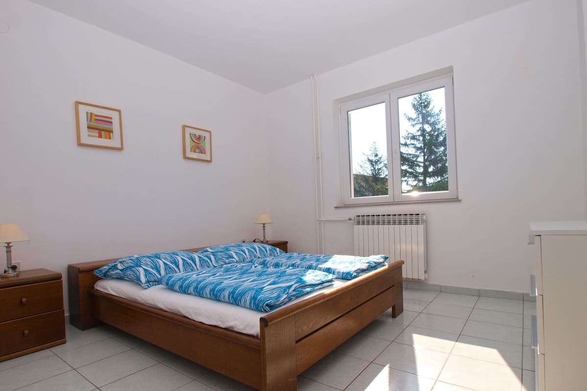 A bedroom with a wooden bed, a nightstand, a window with a view of trees, and a radiator.