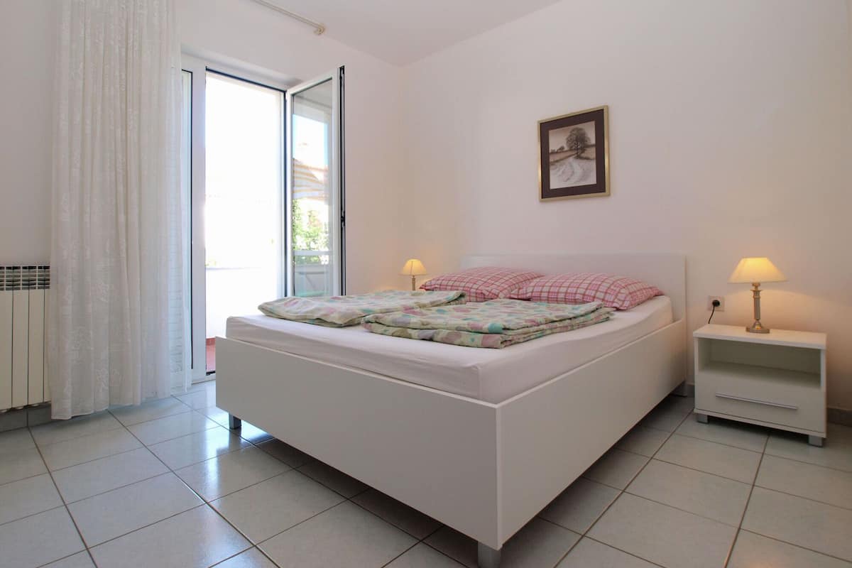 A bedroom with a bed, two bedside tables, a window with curtains, and a wall-mounted picture.