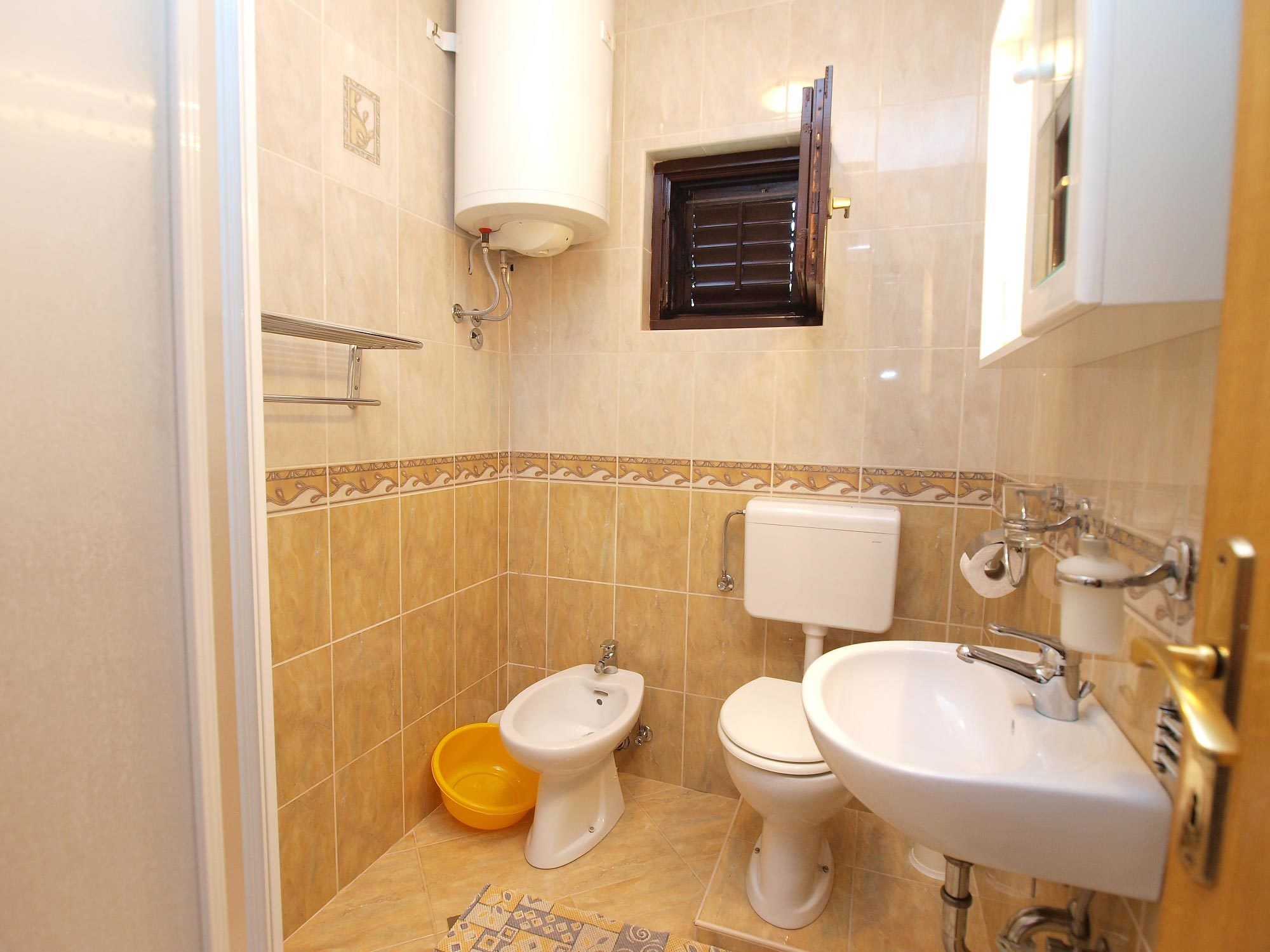 A bathroom with a toilet, bidet, sink, and a small window with blinds.