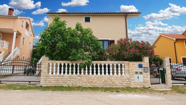 A two-story building with a beige facade, a stone wall with a white balustrade, and a clear blue sky with clouds. - Apartments Lillies 1390 (Fazana)