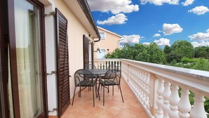 A balcony with a table and chairs, a white balustrade, and a view of greenery and trees. - Apartments Lillies 1390 (Fazana)