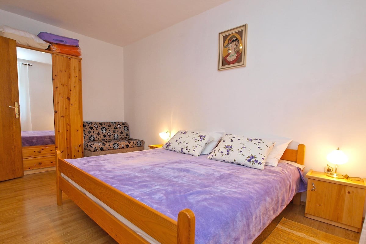 A bedroom with a wooden bed, a sofa, a wardrobe, and a bedside table with a lamp.