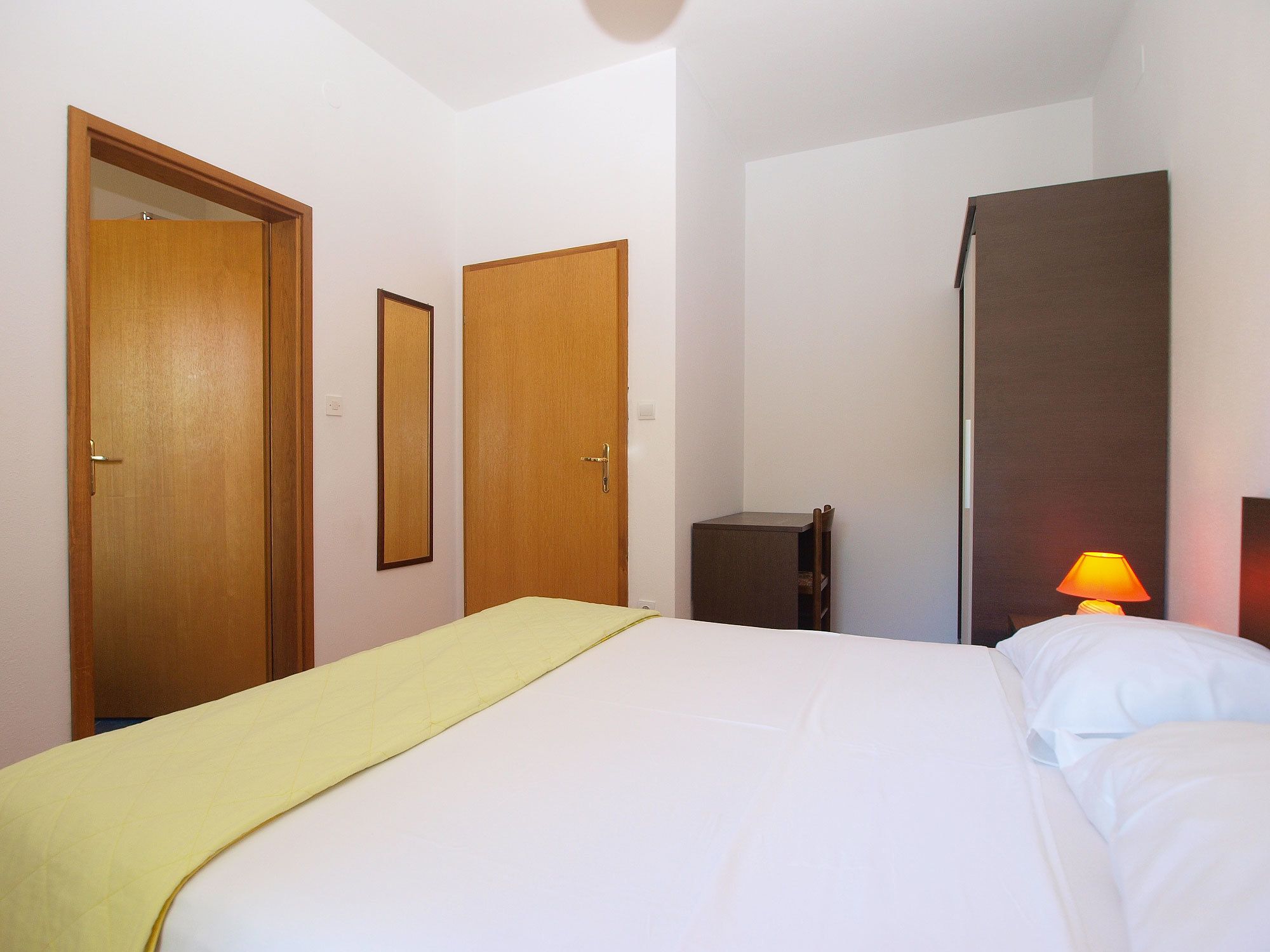 A hotel room with a bed, a bedside table, a lamp, and two doors.