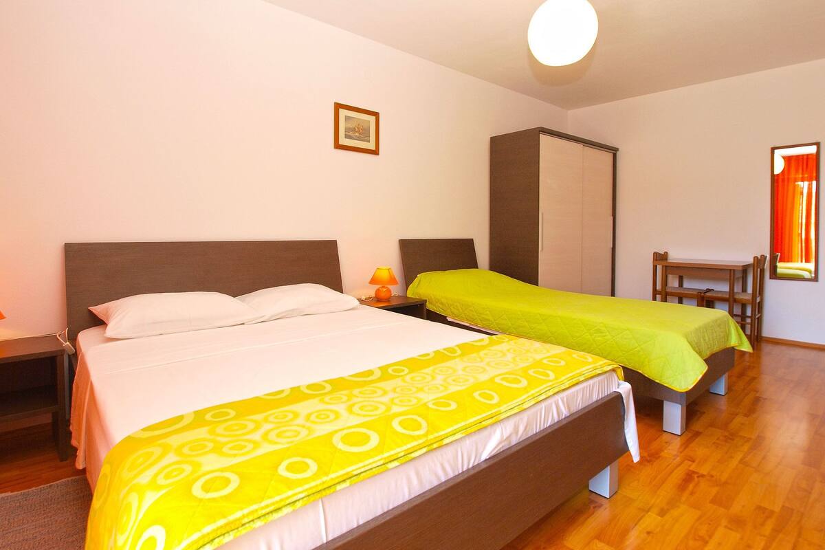 A hotel room with a large bed, a smaller bed, a wardrobe, a desk, and a chair.
