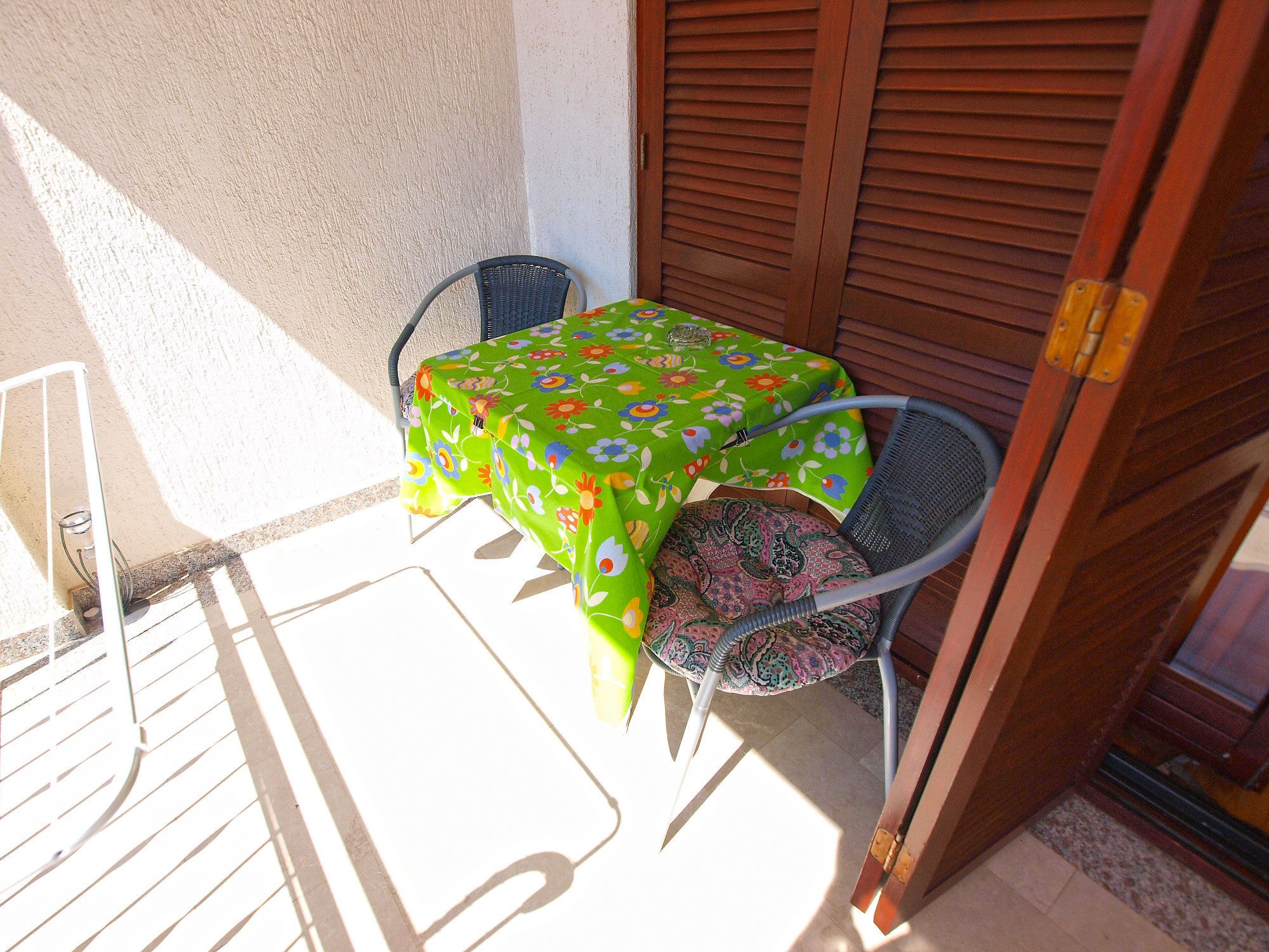 A small outdoor table with a floral tablecloth, a chair, and a wooden door.