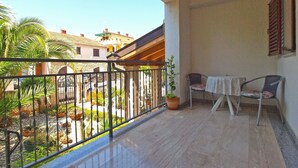 Ein Balkon mit Tisch und Stühlen, einem Blumentopf und Blick auf einen Innenhof mit Pflanzen und einem Gebäude im Hintergrund.
