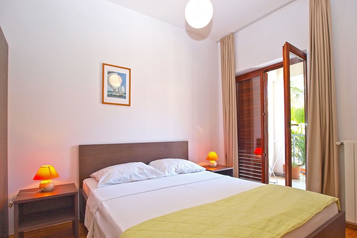 A hotel room with a bed, two bedside lamps, a framed picture on the wall, and a sliding glass door to the outside.