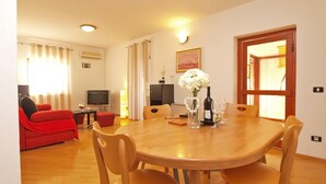A dining area with a wooden table and chairs, a television, a sofa, and a window with curtains. - Apartment Fatima 1514 (Pula)
