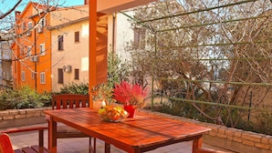 An outdoor patio with a wooden table and chairs, surrounded by a stone wall and a building with orange walls. - Apartment Fatima 1514 (Pula)