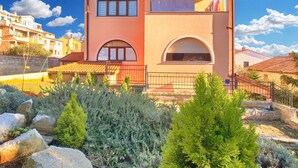 A two-story building with a flat roof, a balcony, and a small garden area with rocks and shrubs. - Apartment Fatima 1514 (Pula)