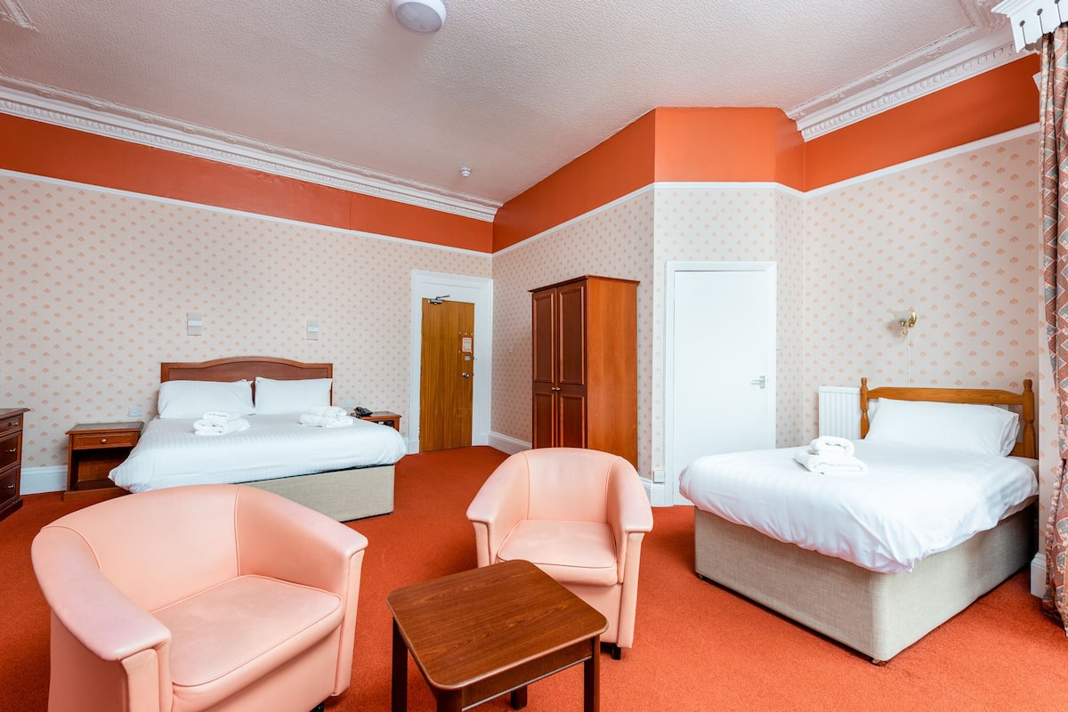 A hotel room with two beds, a wooden headboard, a small table, and two armchairs.