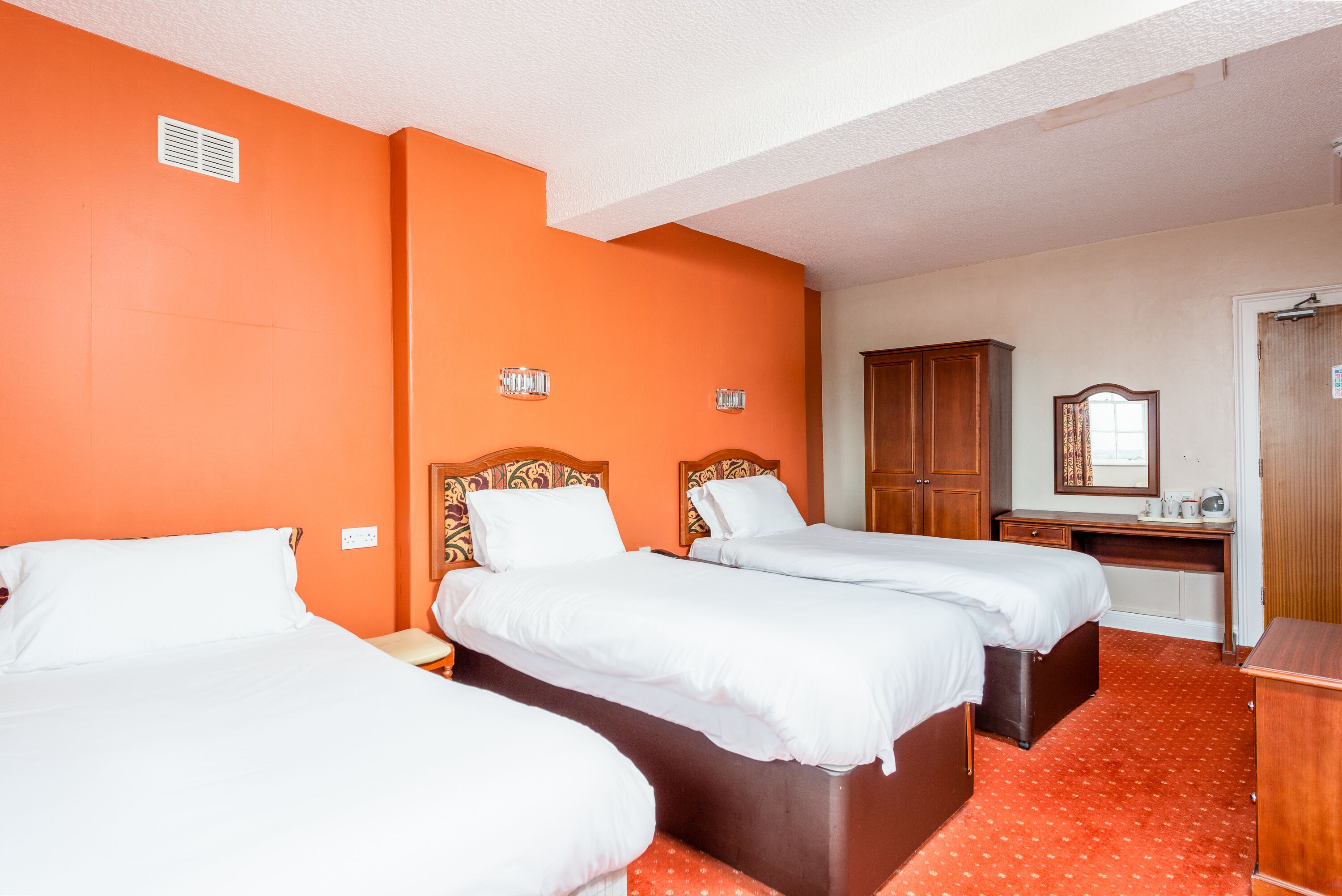 Habitación de hotel con dos camas, un escritorio, un armario y un espejo.