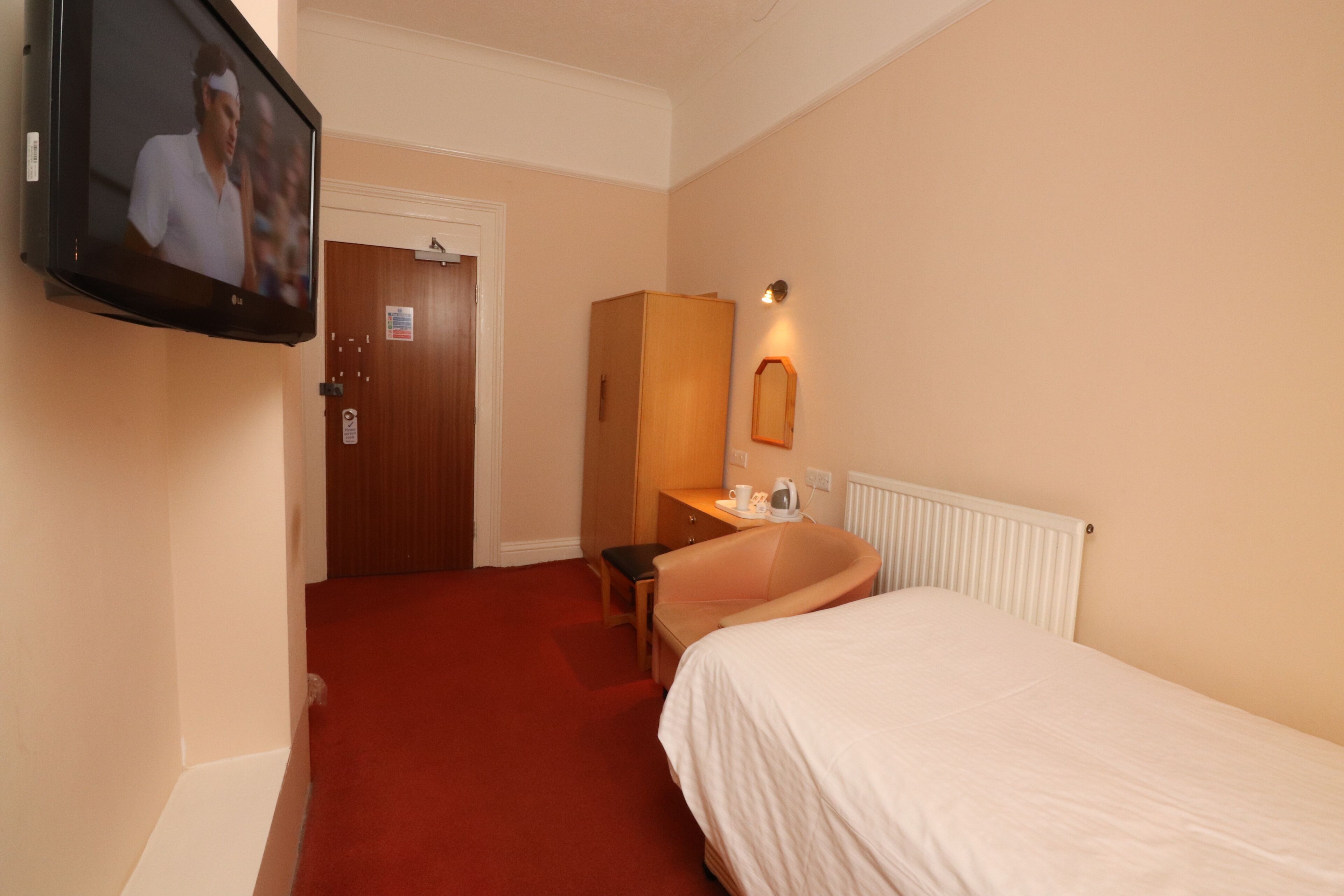 Habitación de hotel con cama, escritorio, silla, televisor y baño con espejo y radiador.