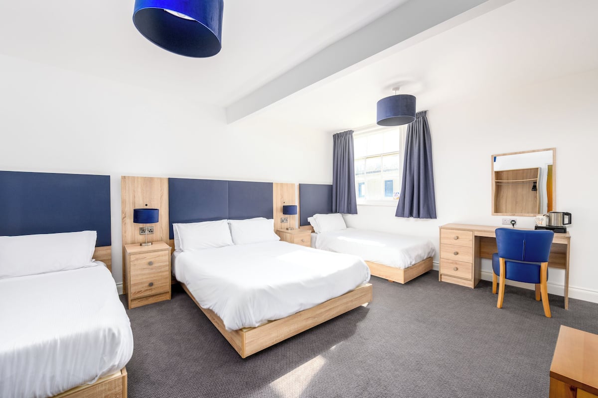 A hotel room with three beds, a desk, and a chair.