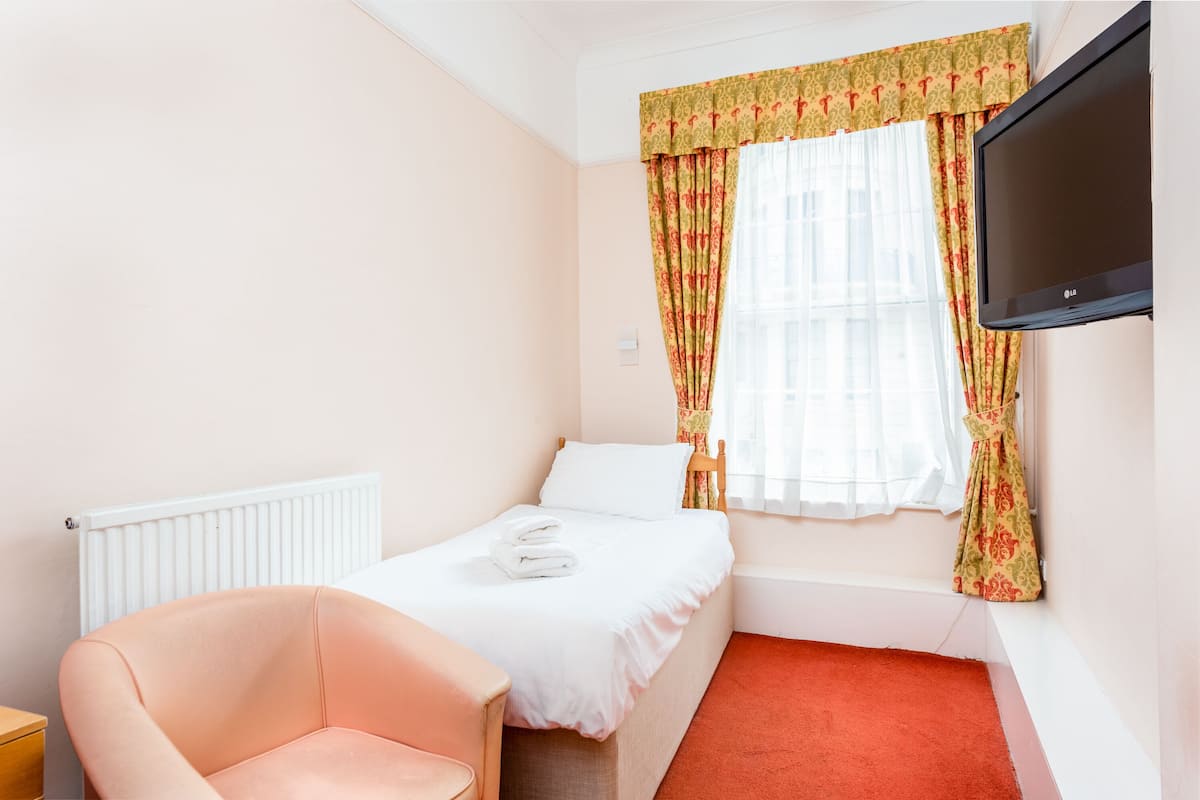 A hotel room with a single bed, a chair, a TV, and a window with curtains.