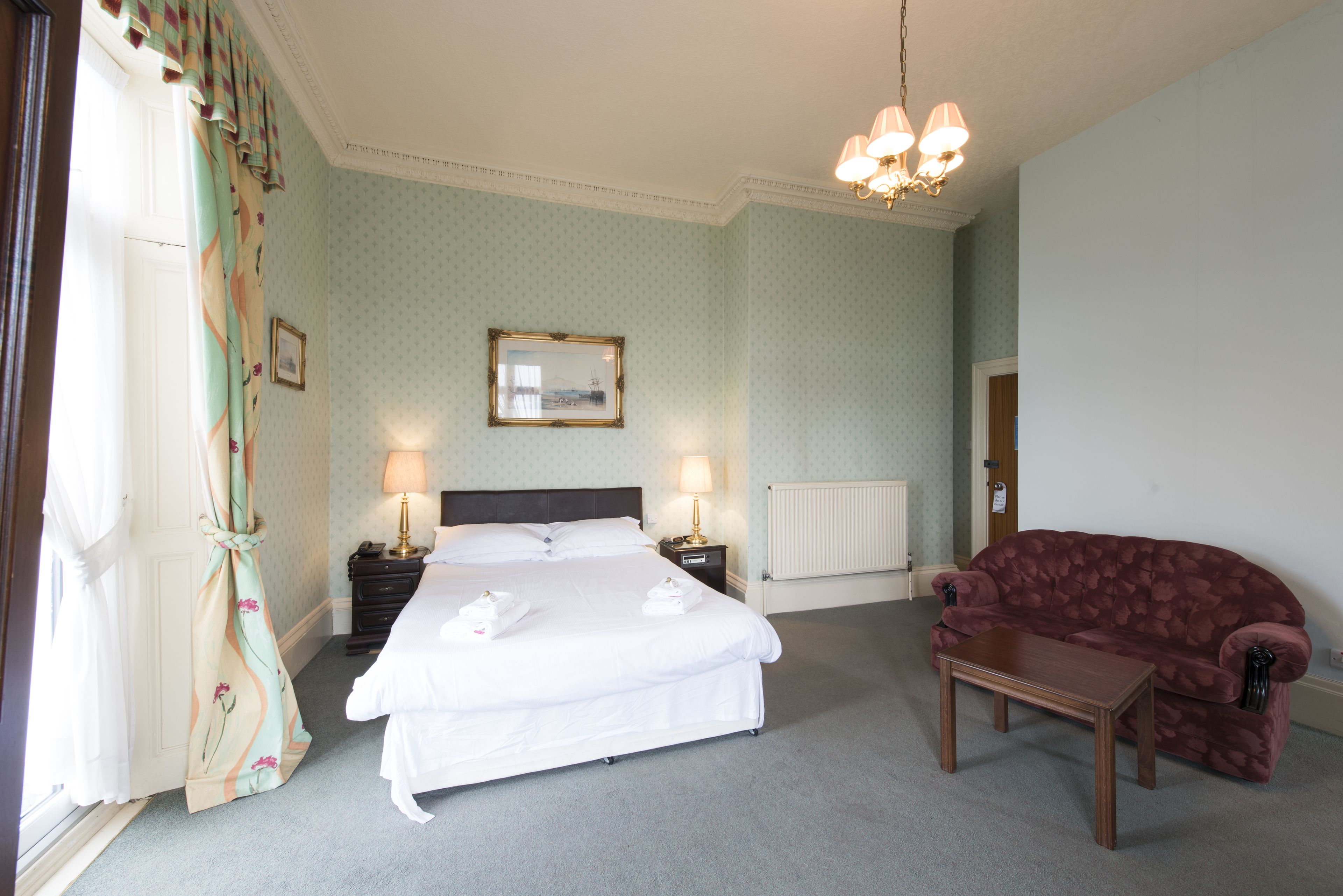 Een hotelkamer met een bed, bedlampen, een rode bank en een kleine tafel.