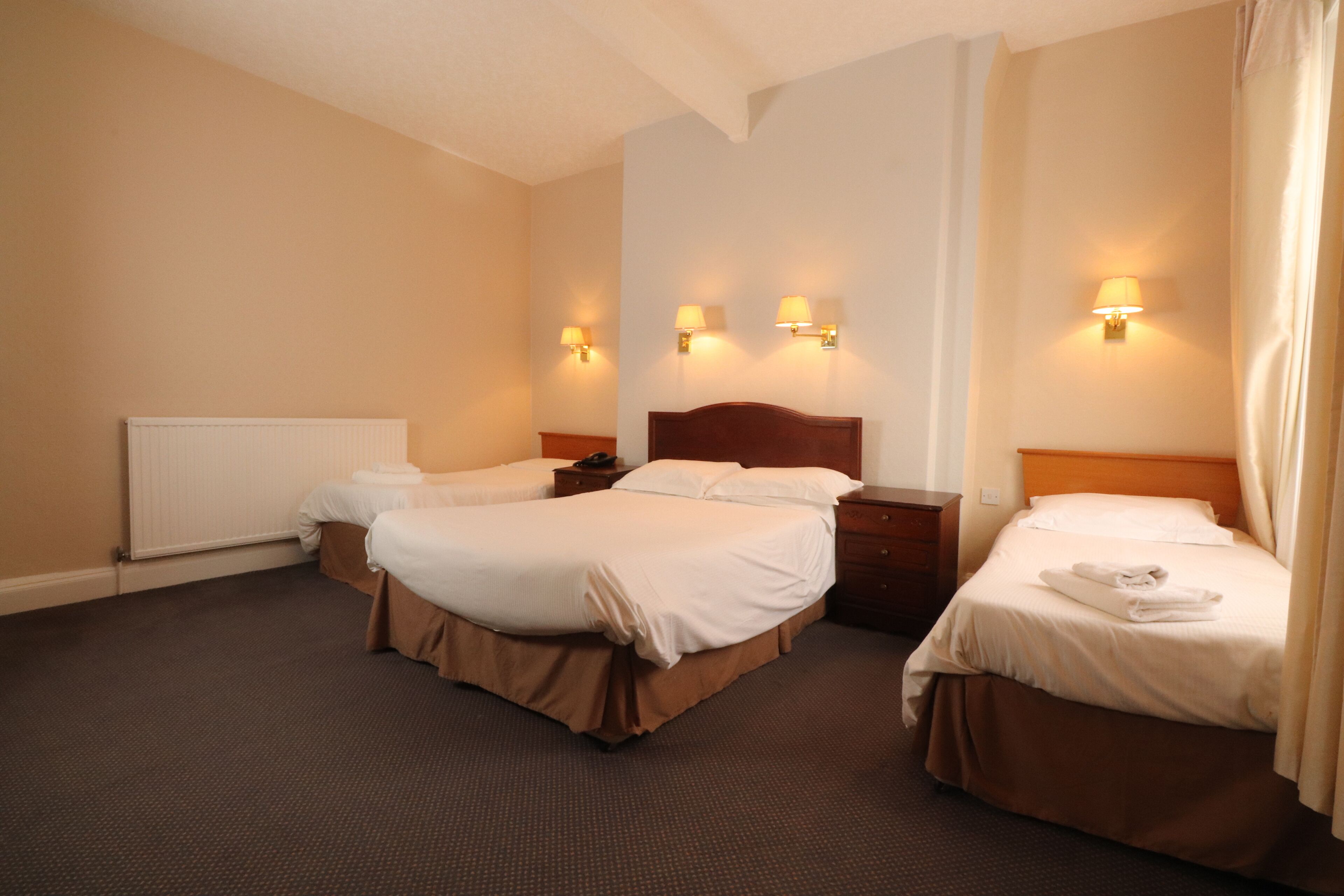 A hotel room with two beds, a wooden headboard, bedside tables, lamps, and a radiator.