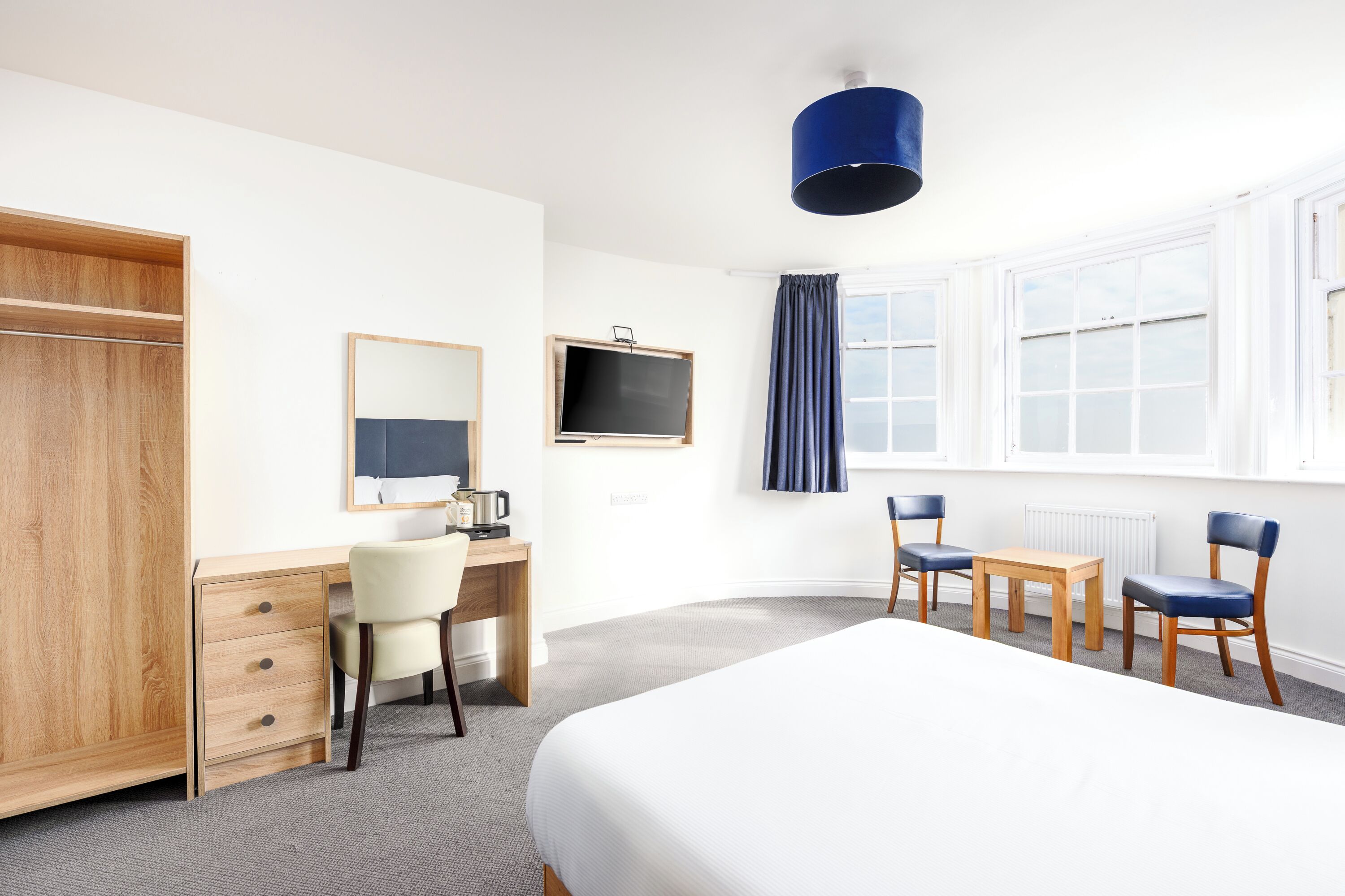 Habitación de hotel con cama, escritorio, silla, armario, televisor y ventana con cortinas.