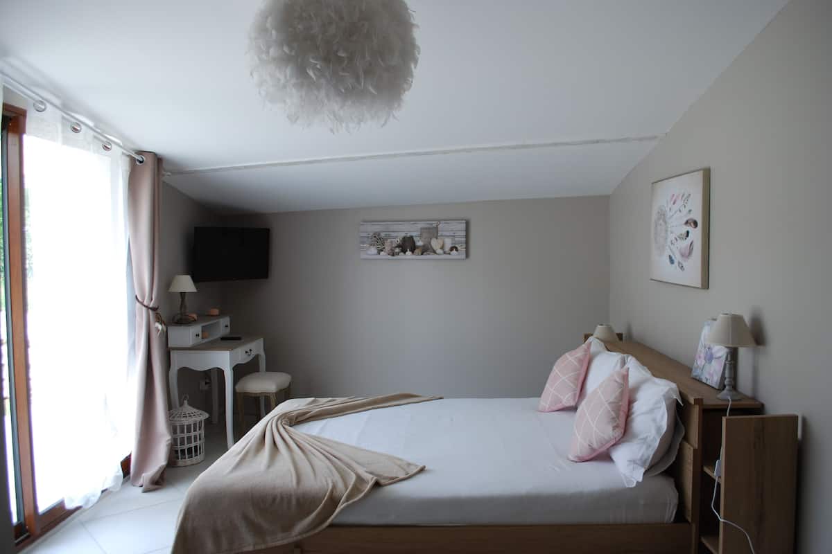 Un dormitorio con cama, mesitas de noche, un escritorio, una silla, una lámpara colgante y una ventana con cortinas.