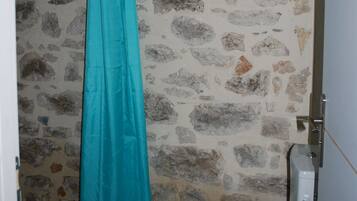 A bathroom with a stone wall, a white toilet, and a turquoise shower curtain.